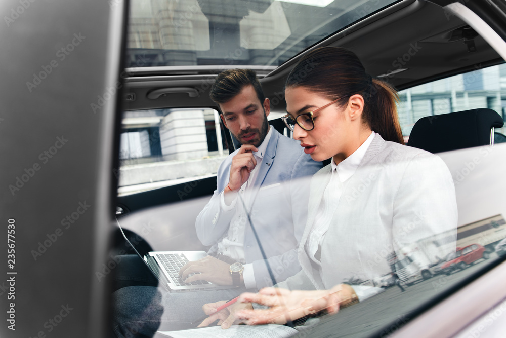 Young business people working together while traveling by a car. They are using laptop and preparing for meeting. Young business people working together while traveling by a car. They are using laptop and preparing for meeting.
