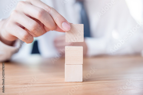 Hand of businessman arranging empty wood cube stacking on top with wooden table. Space for symbol.