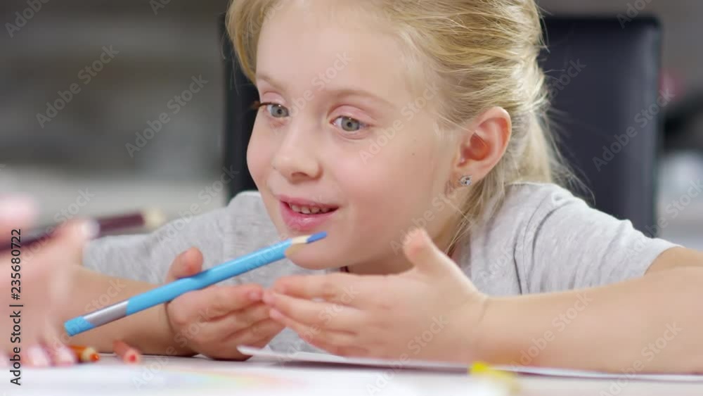 Close-up of cute little girl with blonde hair drawing with colored pencils and telling something to brother Close-up of cute little girl with blonde hair drawing with colored pencils and telling something to brother