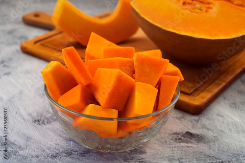 Diced pumpkin in a glass plate. Light background. Raw vegetables. Vegetarian food.