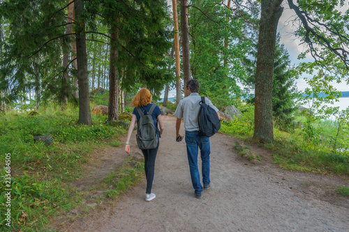 Dark-haired middle-aged man and red-haired young lady walk along forest road. Tourists on the beautiful landscape background. Monrepos Park, Vyborg, Russia. Travel concept © Tatyana_Andreyeva