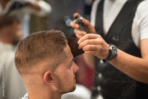 Qualified barber fixating hair of customer with hair spray