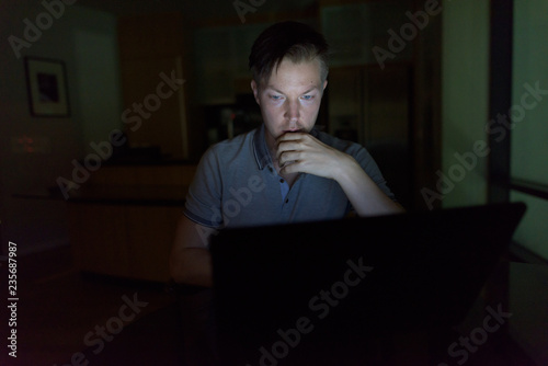 Canvas Print Young handsome man using laptop in the dark living room