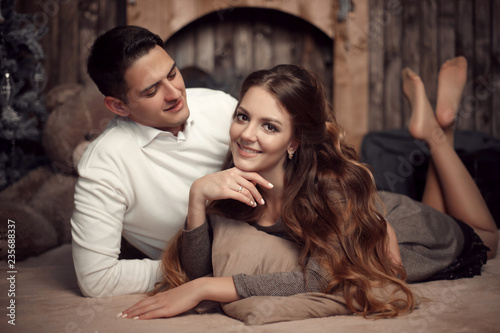 Young happy couple in love lying on rug in cozy wooden interior. Beautiful brunette woman with boyfriend enjoying.