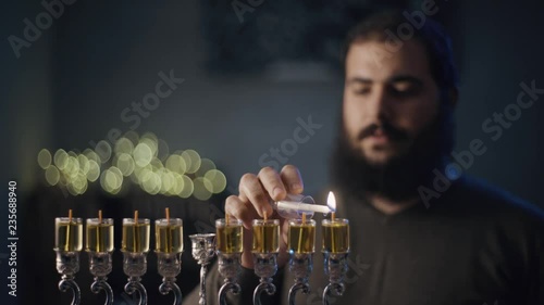 orthodox jewish person light a hanukkah menorah with olive oil candles.