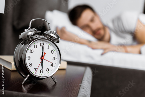 close-up view of alarm clock and young man sleeping behind