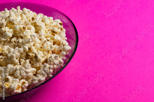 Full glass plate of fried popcorn on pink background with copy space. Concept of leisure
