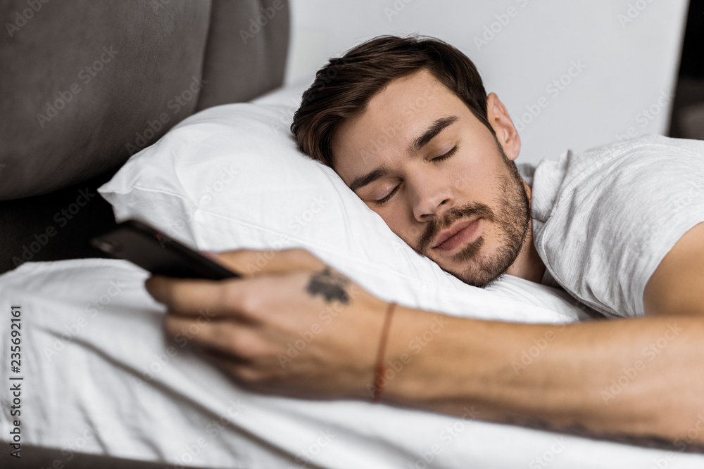 handsome bearded young man sleeping in bed with smartphone in hand handsome bearded young man sleeping in bed with smartphone in hand