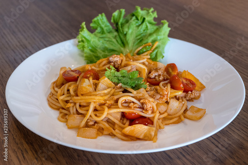 Plate of delicious Italian spaghetti with tomato sauce and fresh basil on wooden table background.
