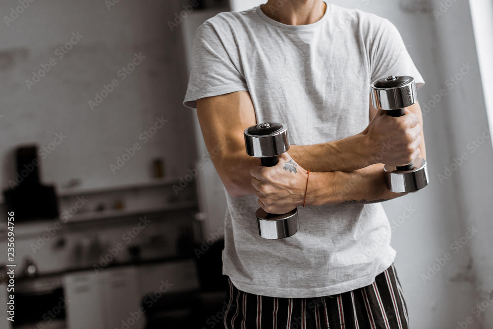 cropped shot of young man in pajamas holding dumbbells at home cropped shot of young man in pajamas holding dumbbells at home