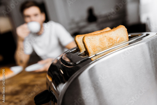 young man drinking coffee at home with toaster on foreground photo