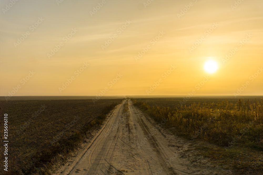 Dirt road along the field and yellow sky