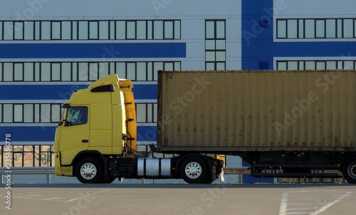 Semi truck with trailer on the asphalt road in front of facade of cargo terminal 