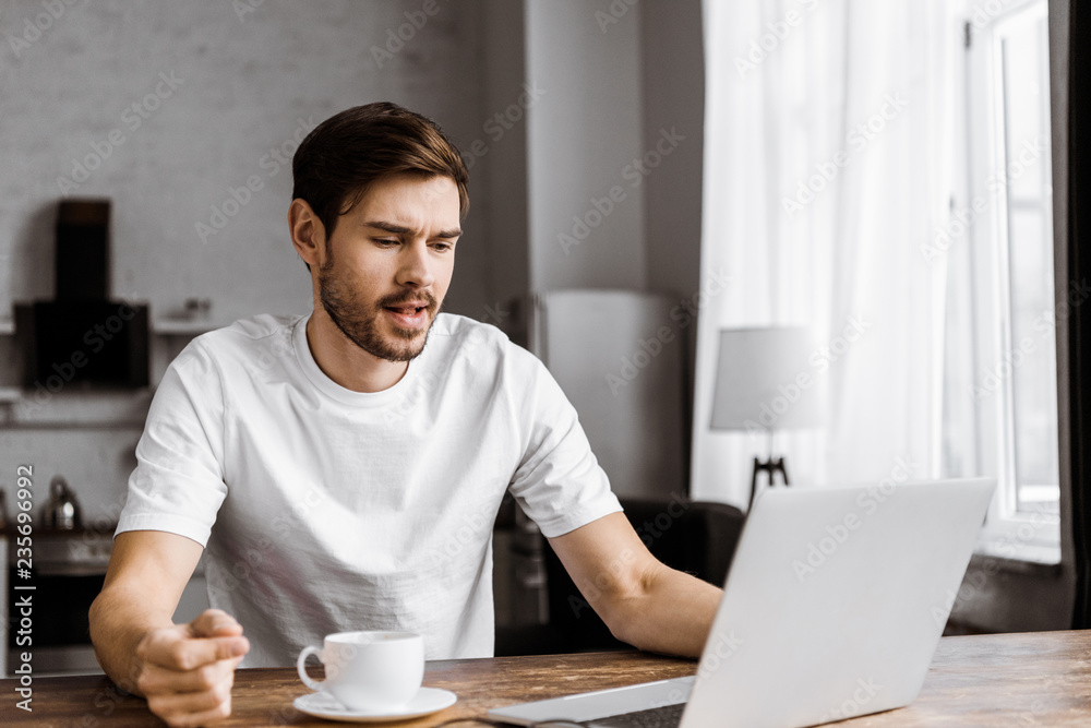 confused young freelancer with coffee using laptop at home confused young freelancer with coffee using laptop at home