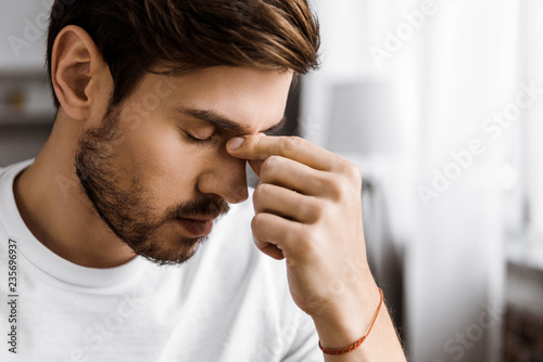 close-up portrait of depressed young man touching nose bridge at home