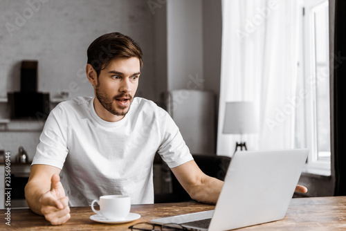 shocked young man with coffee using laptop at home