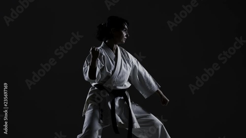 girl practicing karate, wearing kimono, harsh side light against black background