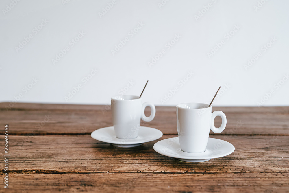 2 Espresso Tassen mit Löffel stehend auf Unterteller Holztisch Hintergrund weiß 2 Espresso Tassen mit Löffel stehend auf Unterteller Holztisch Hintergrund weiß