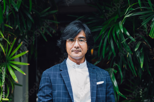 Portrait of elegant Asian middle-aged businessman standing outdoors and looking at camera.