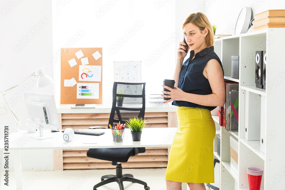 A young girl talking on the phone in the office and holding a glass of coffee. A young girl talking on the phone in the office and holding a glass of coffee.
