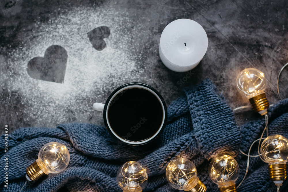  Cup of coffee , candle, notebook, pen and warm woolen sweater , decorated with led lights on gray table.Winter  concept. Flat lay, top view. Valentines day.
