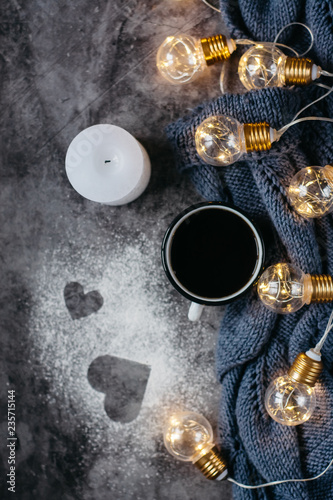  Cup of coffee , candle, notebook, pen and warm woolen sweater , decorated with led lights on gray table.Winter concept. Flat lay, top view. Valentines day.