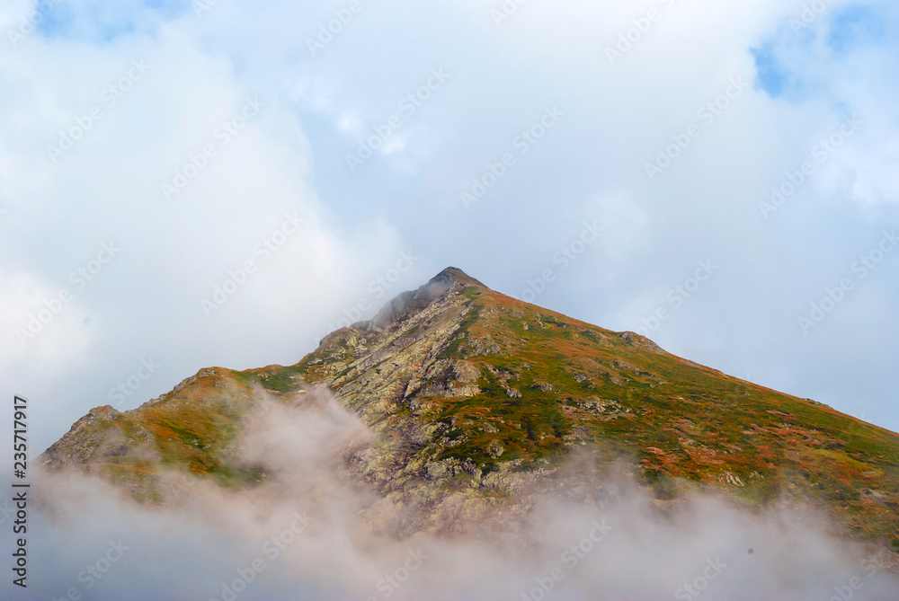 cone-shaped rocky mountain peak with multi-colored vegetation visible in the lumen of the clouds cone-shaped rocky mountain peak with multi-colored vegetation visible in the lumen of the clouds