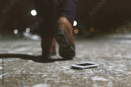 Lost mobile phone dropped from a woman pocket on the night footpath and is walking away silhouette of woman. photo