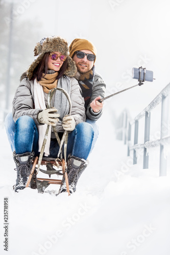 Young couple taking selfies on sledge in snow