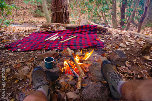 Photo First person view of man relaxing / having tea in an enamel outdoor mug by a campfire in Blue Ridge / Appalachian Mountains trail near Asheville, North Carolina