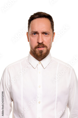 Portrait of handsome man with stubble has indignant expression, frowns face, dressed in white shirt, isolated over white background.