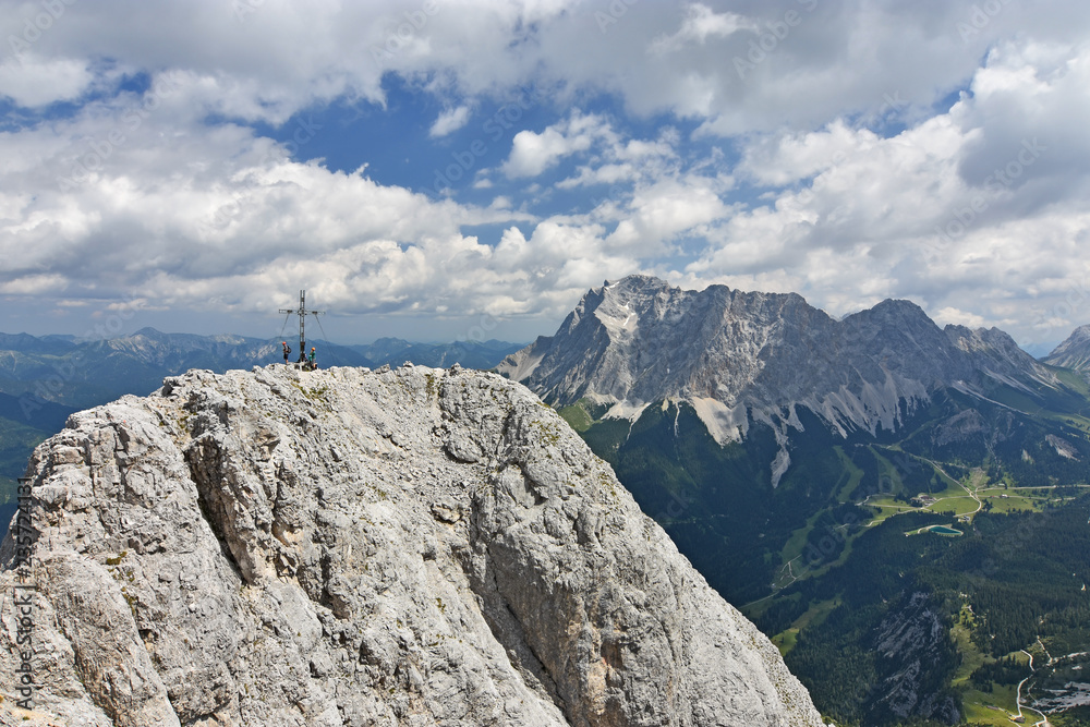 Obraz premium Climbers at the summit of a mountain (Ehrwalder Sonnenspitze) near Ehrwald, Tyrol, Austria. Wetterstein mountain range with Zugspitze in the background