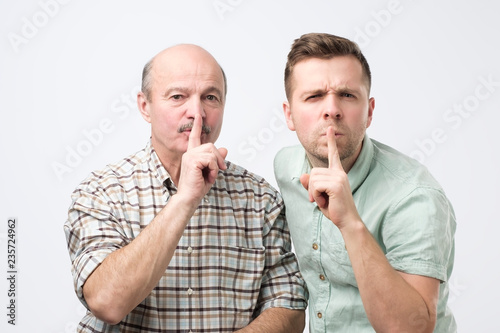 Two mature men keep fore finger on lips, tries to keep conspiracy photo