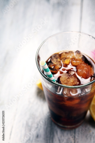 Softdrink with ice cubes, lemon and straw in glass