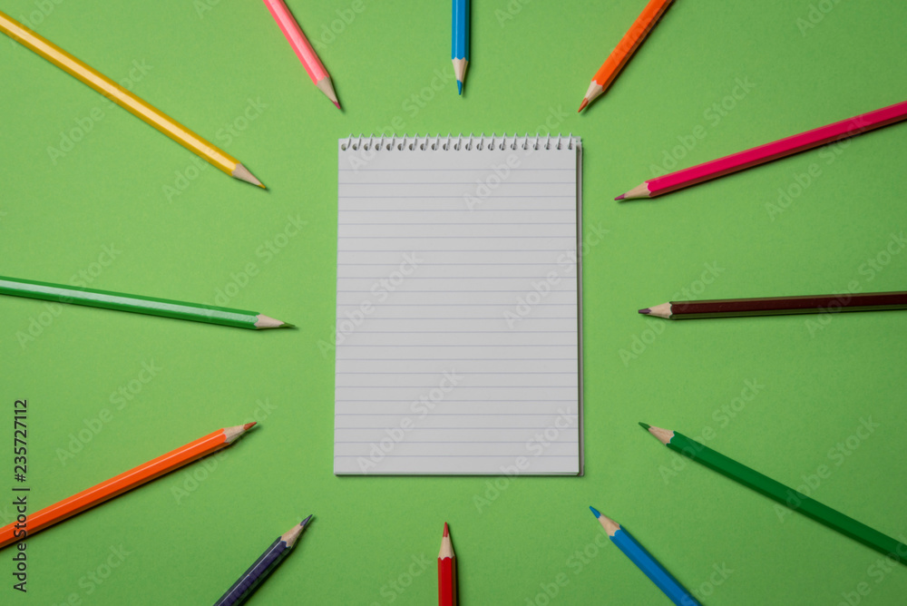 Blank notebook and colored pencils on a green background. Above view Blank notebook and colored pencils on a green background. Above view