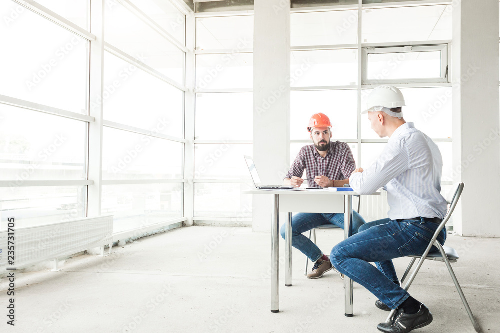 male engineers, architects working at the desk in helmets. Drawings, laptop, roulette on the desktop. Reception and supervision of building construction