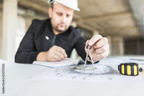 architect builder works at the table with drawings. Helmet, drawings, compasses in the workplace