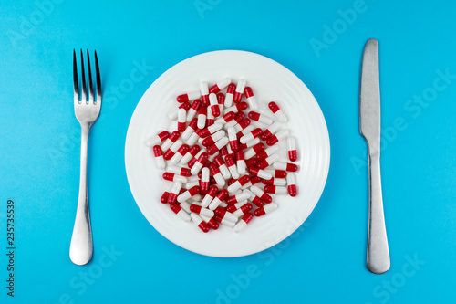 pharmaceutical medicine pills or capsules on a plate with a fork and knife. top view blue background. appetite suppressants for dieting concept photo