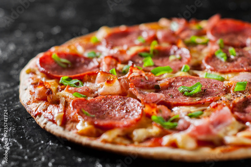 Pepperoni Pizza with Mozzarella cheese, salami, bacon, Tomato sauce, pepper, Spices and Fresh green onion. Italian pizza on black background