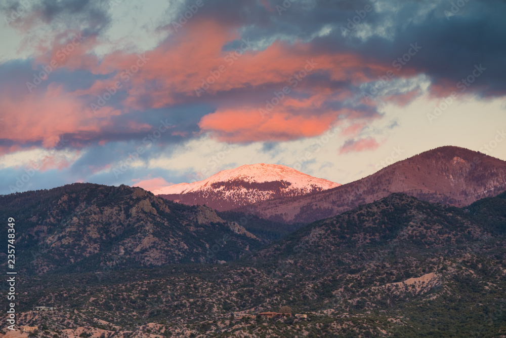 Obraz premium Dramatyczny, piękny zachód słońca rzuca fioletowe i pomarańczowe kolory na chmury i ośnieżony szczyt Santa Fe Baldy nad dzielnicą Tesuque, niedaleko Santa Fe w Nowym Meksyku