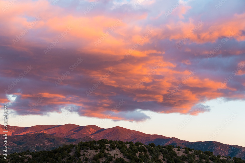 Naklejka premium Dramatyczny, piękny zachód słońca rzuca fioletowe i pomarańczowe kolory na chmury i góry Sangre de Cristo w pobliżu Santa Fe w Nowym Meksyku
