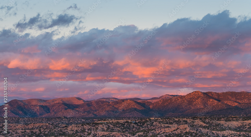Naklejka premium Dramatyczny, piękny zachód słońca rzuca fioletowe i pomarańczowe kolory i odcienie na chmury i góry nad okolicą w Tesuque, niedaleko Santa Fe w Nowym Meksyku
