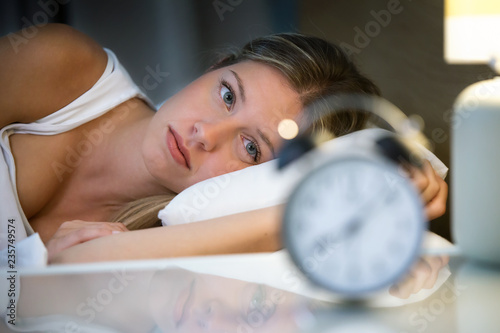 Beautiful young exhausted woman suffering insomnia lying on bed in bedroom at home. photo