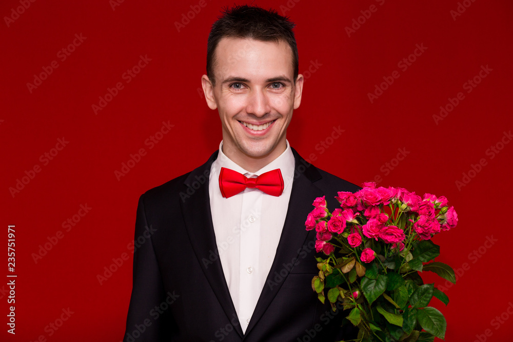 Stylish man in suit holding a bouquet of flowers isolated on red Stylish man in suit holding a bouquet of flowers isolated on red