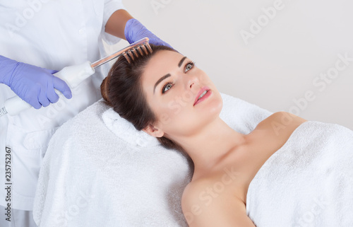 The doctor-cosmetologist makes the procedure Microcurrent therapy On the hair of a beautiful, young woman in a beauty salon.Cosmetology and professional skin care. photo