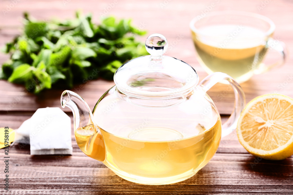 Glass teapot with lemon and mint leafs on wooden table Glass teapot with lemon and mint leafs on wooden table