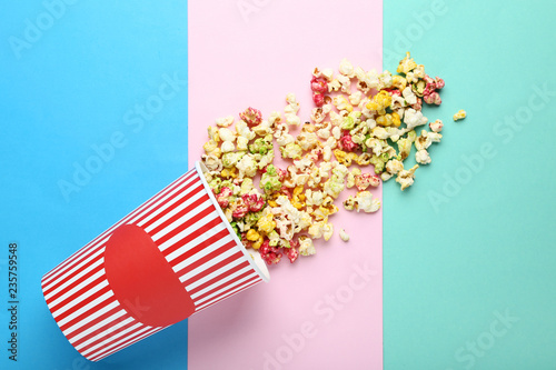 Sweet popcorn in striped bucket on colorful background