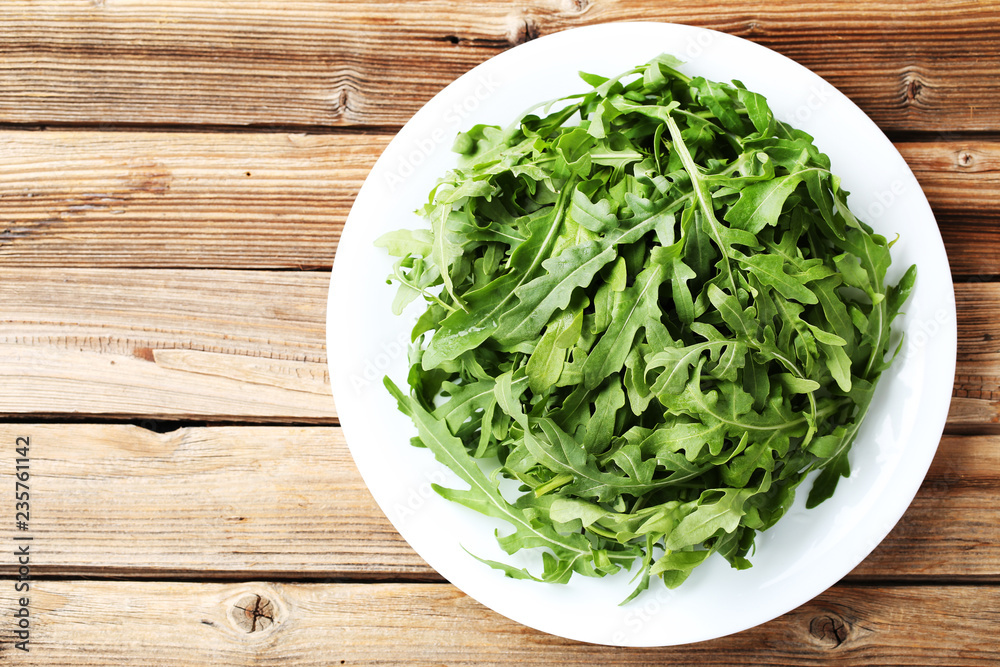 Green arugula leafs in plate on brown wooden table Green arugula leafs in plate on brown wooden table