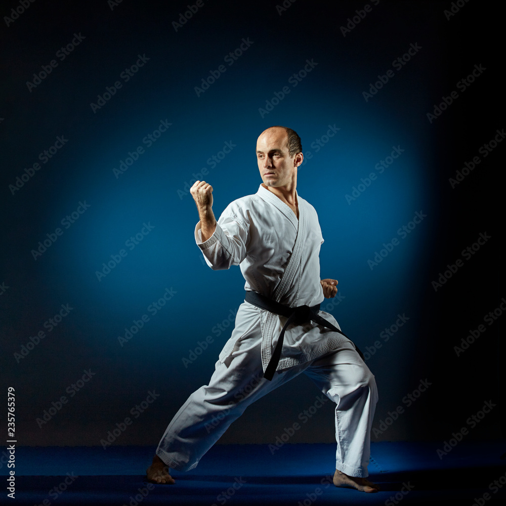 On the blue tatami sportsman performs formal karate exercises