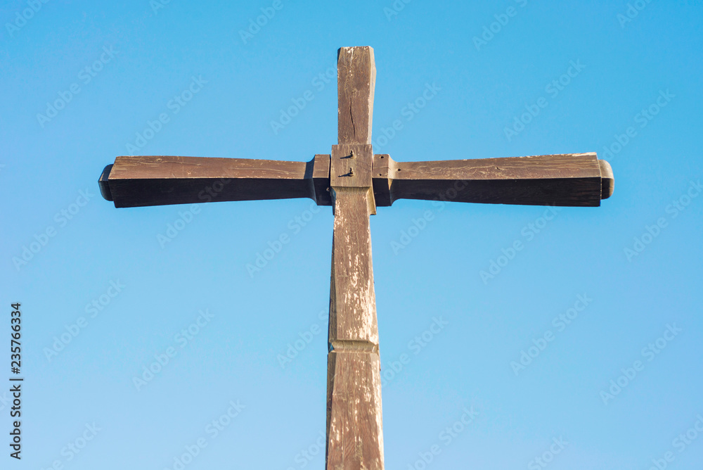 Concept or conceptual wood cross or religion symbol shape over a blue sky. Simple wooden Christian cross against a blue sky Concept or conceptual wood cross or religion symbol shape over a blue sky. Simple wooden Christian cross against a blue sky